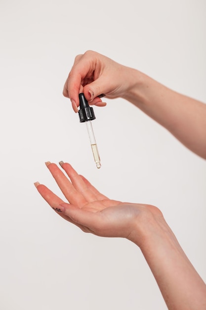 Girl holding a pipette and oil drops in her hands on a white background closeup Beauty and skin care