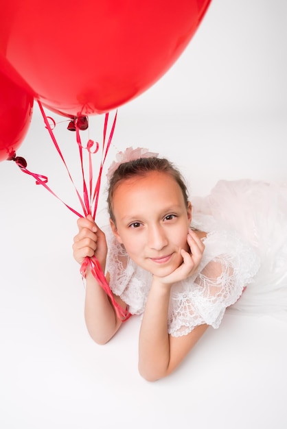 Girl holding red balloons in hand and positive looking at camera lying down on white background