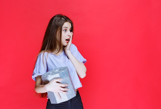 Girl holding a silver gift box and looks depressed and confused. 