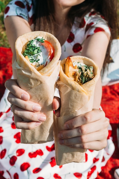 Girl holding two pita or shawarma on the street in summer against the background of the grass