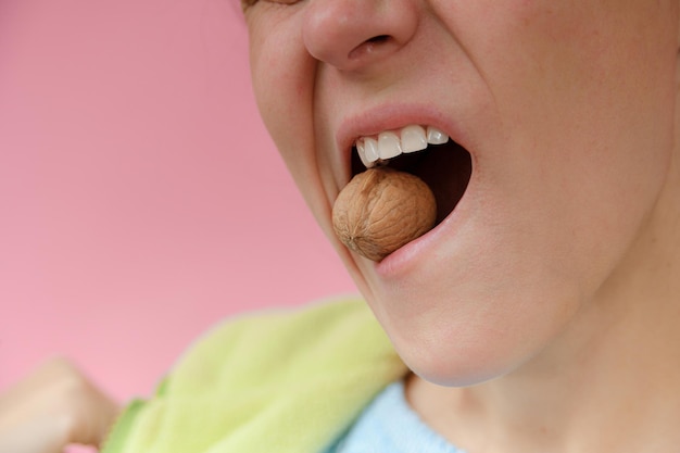 Photo girl holding walnuts with white teeth on a pink background