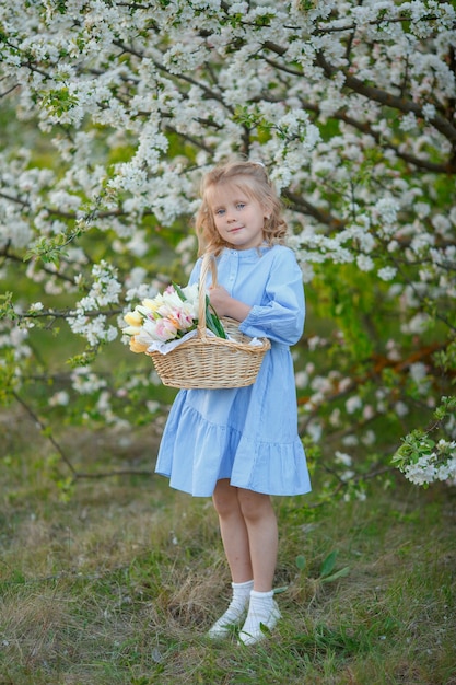 A girl holds a basket of flowers near a flowering tree