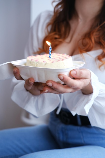 A girl holds a bento cake in her hands with a burning candle in the middle