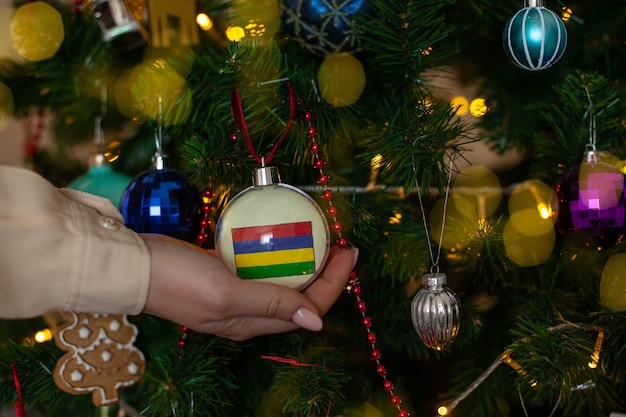 A girl holds a decoration on a fir tree with the flag of Mauritius