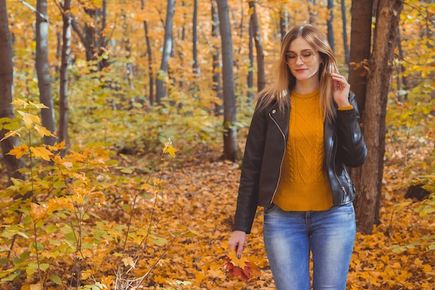 Girl holds fallen leaves and walks in autumn park copy space and place for text seasonal concept