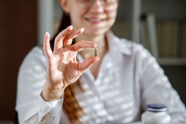 The girl holds a fish oil capsule in her hand Omega3 capsules on the table and in the doctors hand