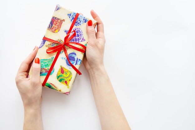 The girl holds a gift in her hands with a red ribbon and multicolored paper on a white background Time to wrap presents Surprise Christmas and New Year concept