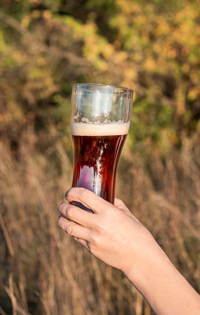 The girl holds a glass glass in her hands into which dark beer is poured