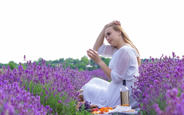 A girl holds a glass of white wine against the backdrop of a lavender field A girl drinks wine in a lavender field