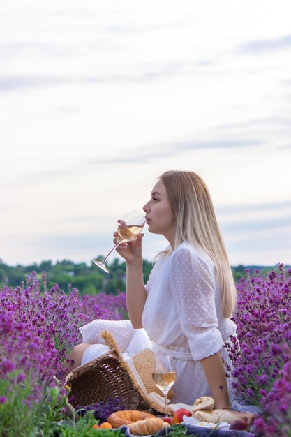 A girl holds a glass of white wine against the backdrop of a lavender field A girl drinks wine in a lavender field