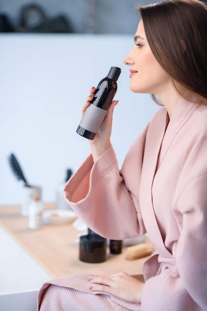 The girl holds a hair care product and sniffes it with her eyes open.