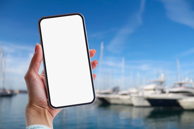 Girl holds in her hand a smartphone with white screen against the backdrop of the sea and yachts.