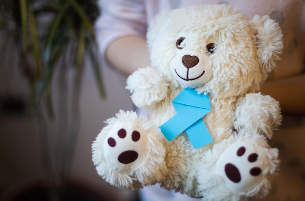 The girl holds in her hands a toy teddy bear with a blue ribbon