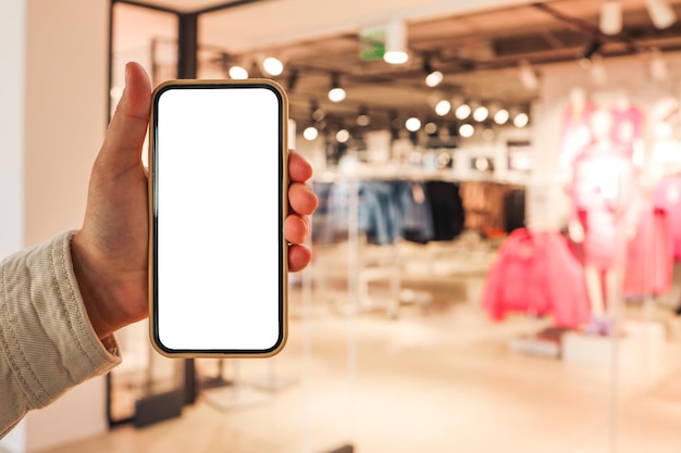 A girl holds a phone in her hand with a blank isolated screen on the background of a blurred shopping center