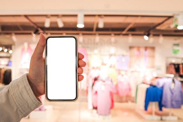 A girl holds a phone in her hand with a blank isolated screen on the background of a blurred shopping center