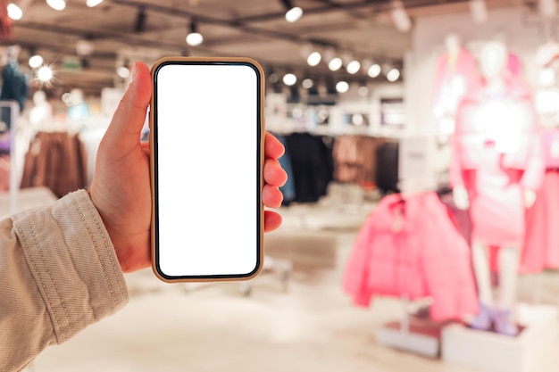 A girl holds a phone in her hand with a blank isolated screen on the background of a blurred shopping center