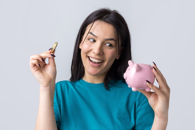 The girl holds a pink piggy bank and a coin in her hands. The concept of wealth and accumulation.