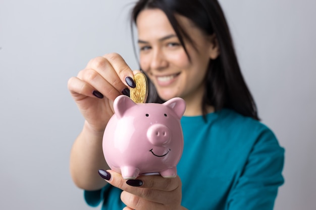 The girl holds a pink piggy bank and a coin in her hands. The concept of wealth and accumulation.