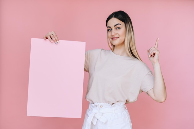 The girl holds a sheet of pink paper in her right hand and index finger points up with her left hand