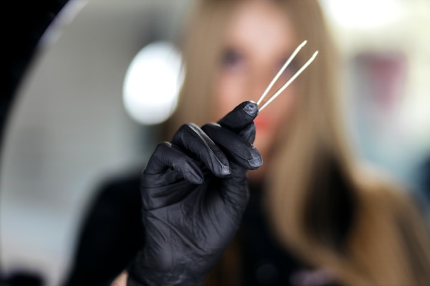 The girl holds tweezers in her hands The girl in black gloves Closeup of a beautiful girl holding an eyebrow tweezer in her hand near her face in the studio