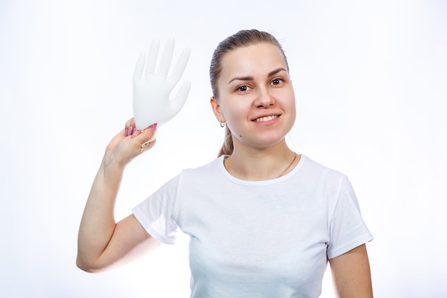 The girl holds white medical gloves in her hands. Protection against germs and the virus. She is in a white T-shirt on a white background.