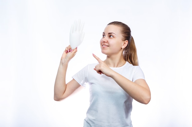 The girl holds white medical gloves in her hands. Protection against germs and the virus. She is in a white T-shirt on a white background.