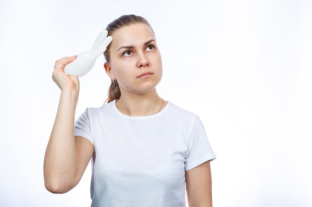 The girl holds white medical gloves in her hands. Protection against germs and the virus. She is in a white T-shirt on a white background.