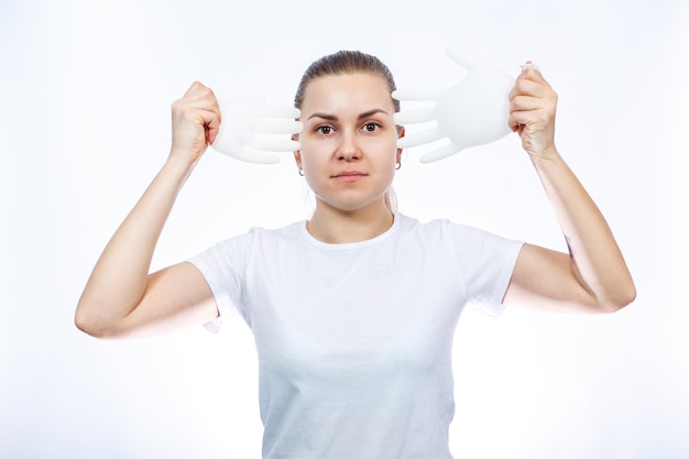 The girl holds white medical gloves in her hands. Protection against germs and the virus. She is in a white T-shirt on a white background.