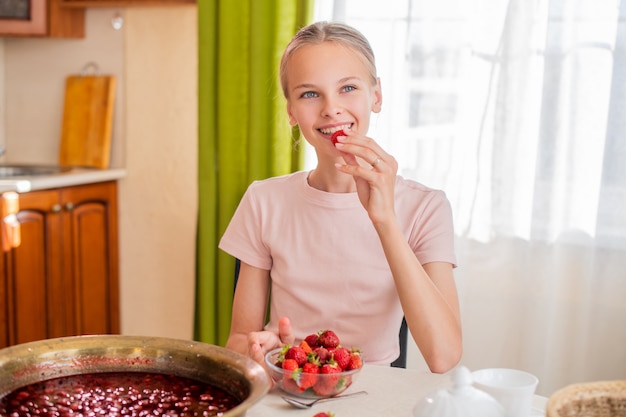 girl at home in the kitchen sits at a table, eats strawberries