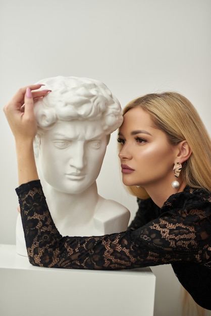 Photo girl hugs a bust of david on a white background