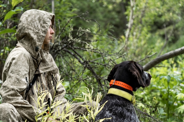 A girl hunter sits with her dog in the bushes. A girl hunts with a German drathaar