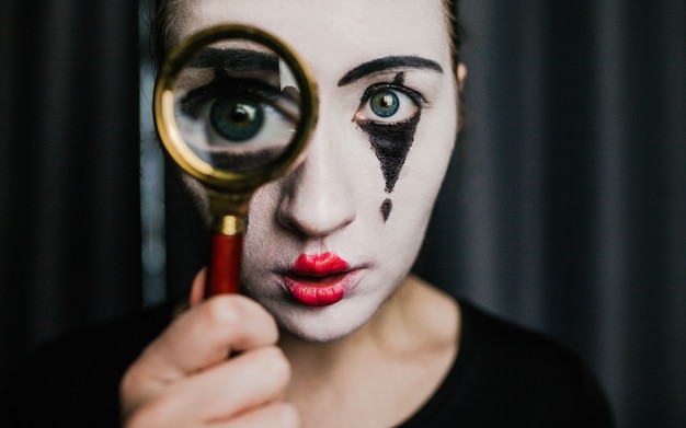 A girl in the image of a mime holds a magnifier.