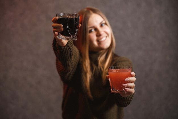 The girl is dressed in a green sweater and holds in her hands glassful with red and black liquid.