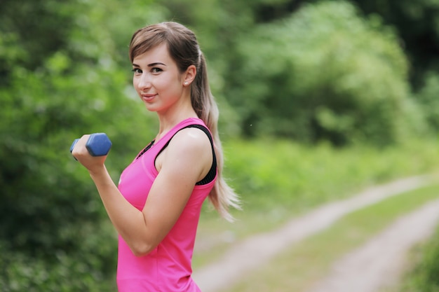 The girl is engaged in sports with weights in nature forest. Healthy fit living