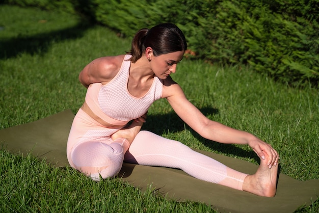 A girl is engaged in yoga on the street, in a pink tracksuit does various exercises and yoga poses