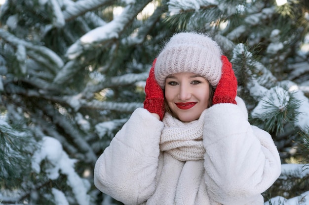 Girl is enjoying frosty winter day in the park Portrait of young woman on snowy pine trees background