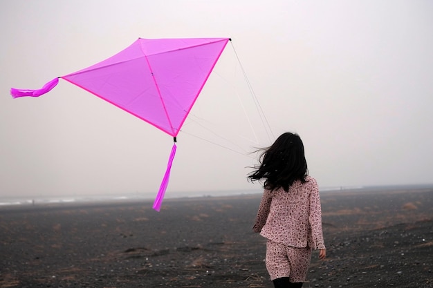 Photo a girl is flying a pink kite with a pink triangle on the bottom