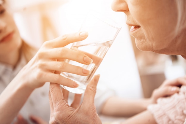 Girl is helping woman with glass of water.