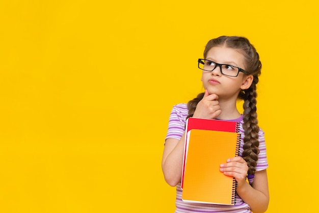 The girl is holding a book and looking away Cute little girl on yellow isolated background