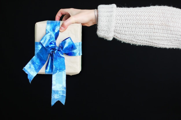 The girl is holding a gift with a blue bow in her hands. Gift in craft paper. Beautiful blue bow.