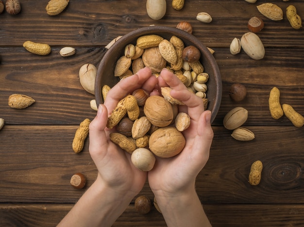 The girl is holding a lot of different nuts on the background of the table. Vegetarian food.