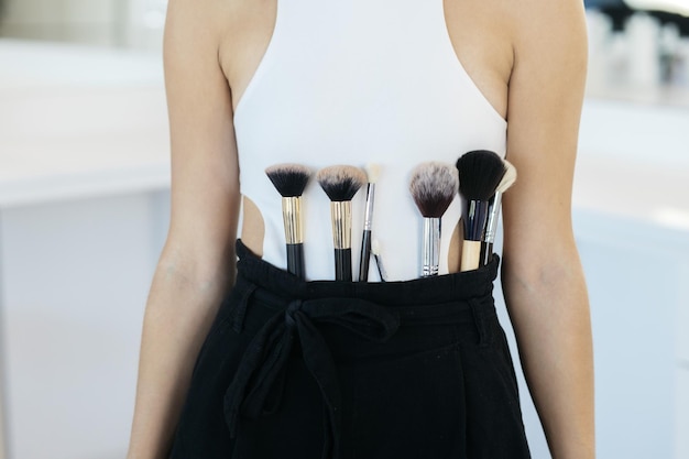 The girl is holding makeup tools Professional makeup artist with a belt bag with tassels makeup brushes Professional Makeup artist doing glamour model makeup at work