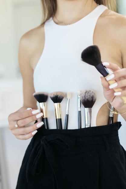 The girl is holding makeup tools Professional makeup artist with a belt bag with tassels makeup brushes Professional Makeup artist doing glamour model makeup at work