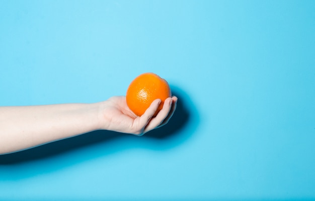 The girl is holding an orange on a blue background.