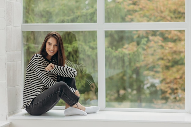 The girl is at home a young girl sits on the windowsill Happy girl