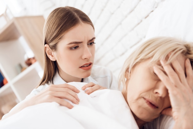 Girl is nursing elderly woman in bed at home.