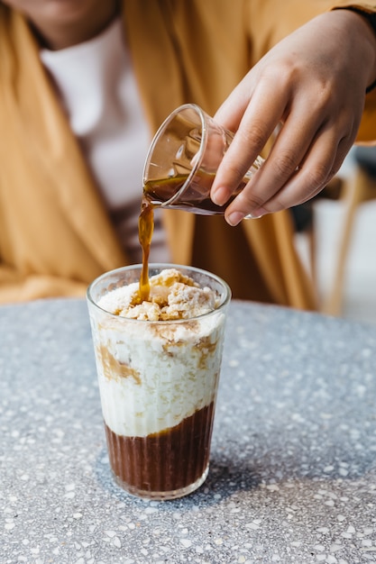 A girl is pouring a shot of espresso in frozen milk mixed with coffee jelly on granite top table. Coffee aroma with fresh milk and chewy coffee jelly.