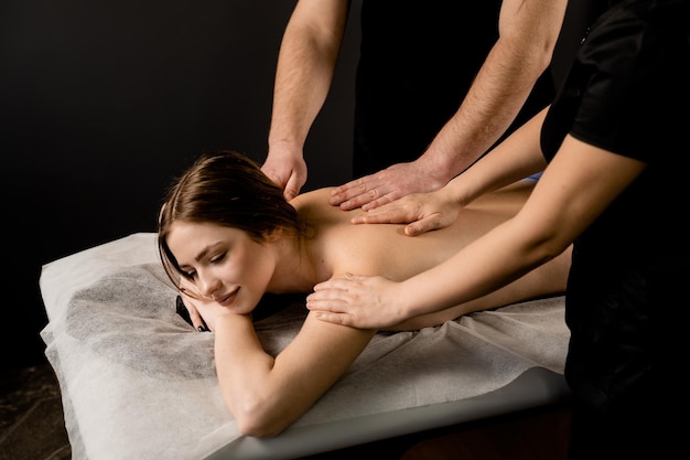 Girl is relaxing on four hands classic massage in spa Two masseurs are making 4 hands massage using massage oil Spa beauty procedures