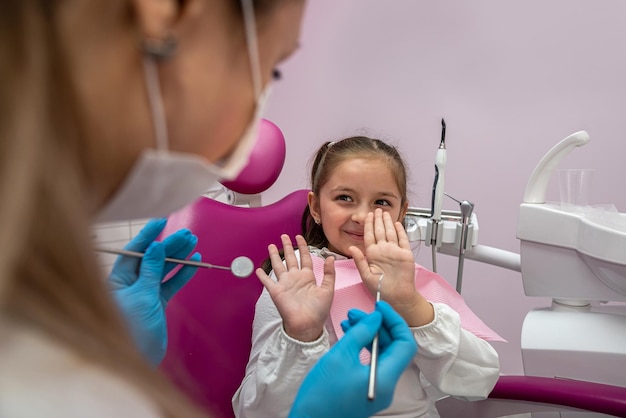 Girl is sitting dental chair does not want to treat her teeth by showing appropriate gestures