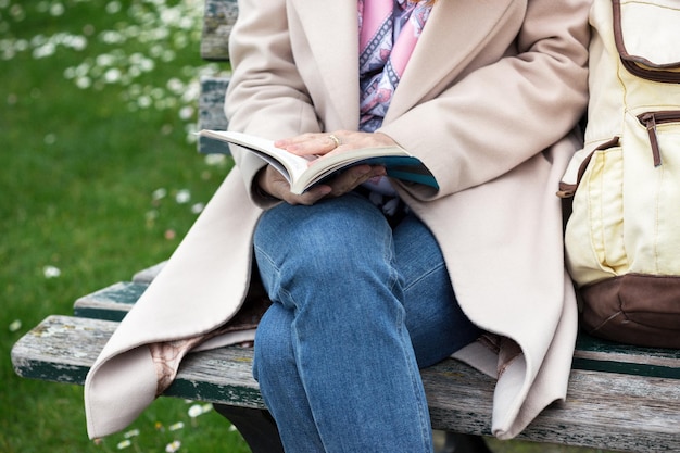 The girl is sitting on a park bench and reading a book